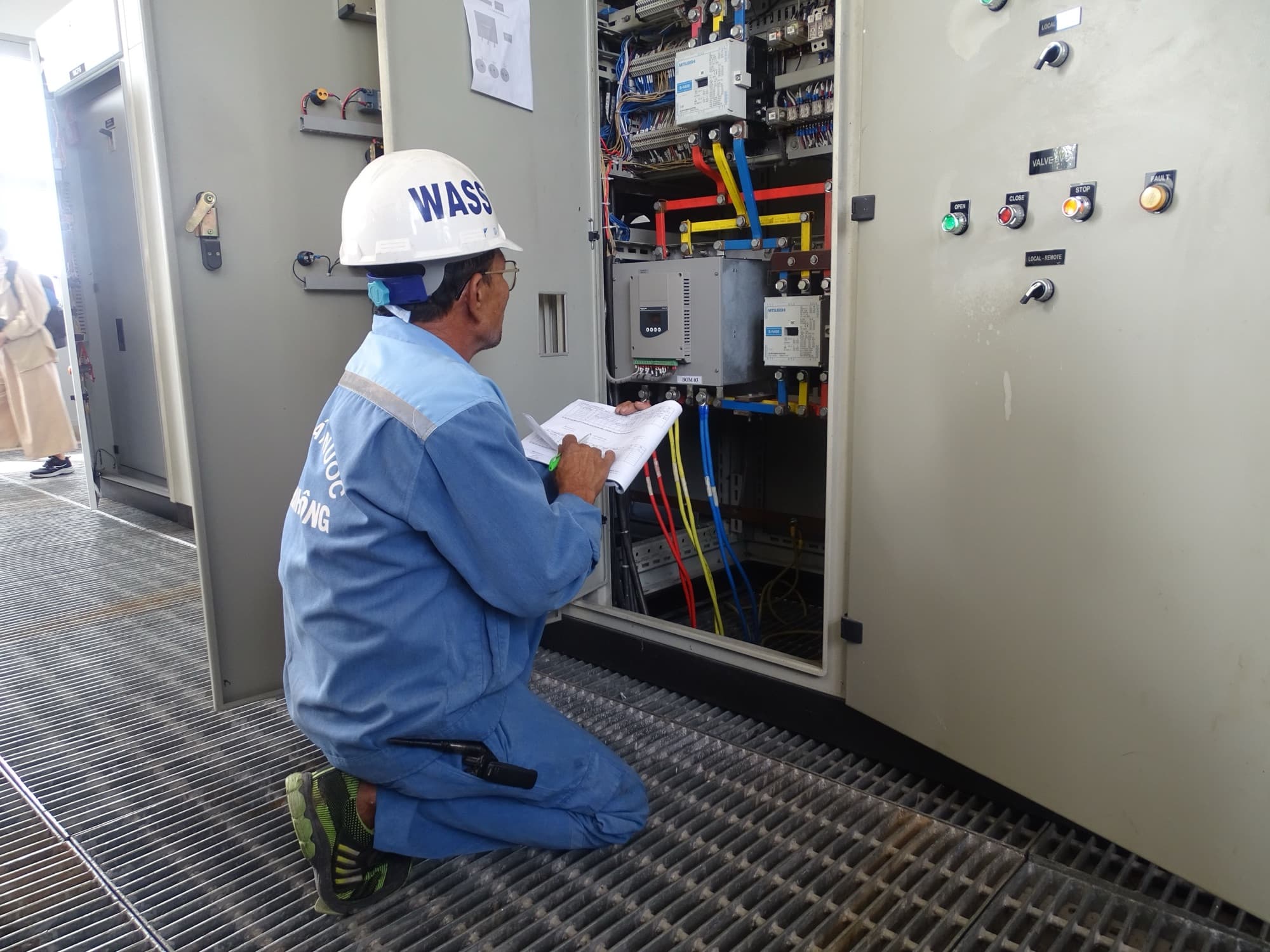 Technician in a hard hat inspecting an electrical control cabinet